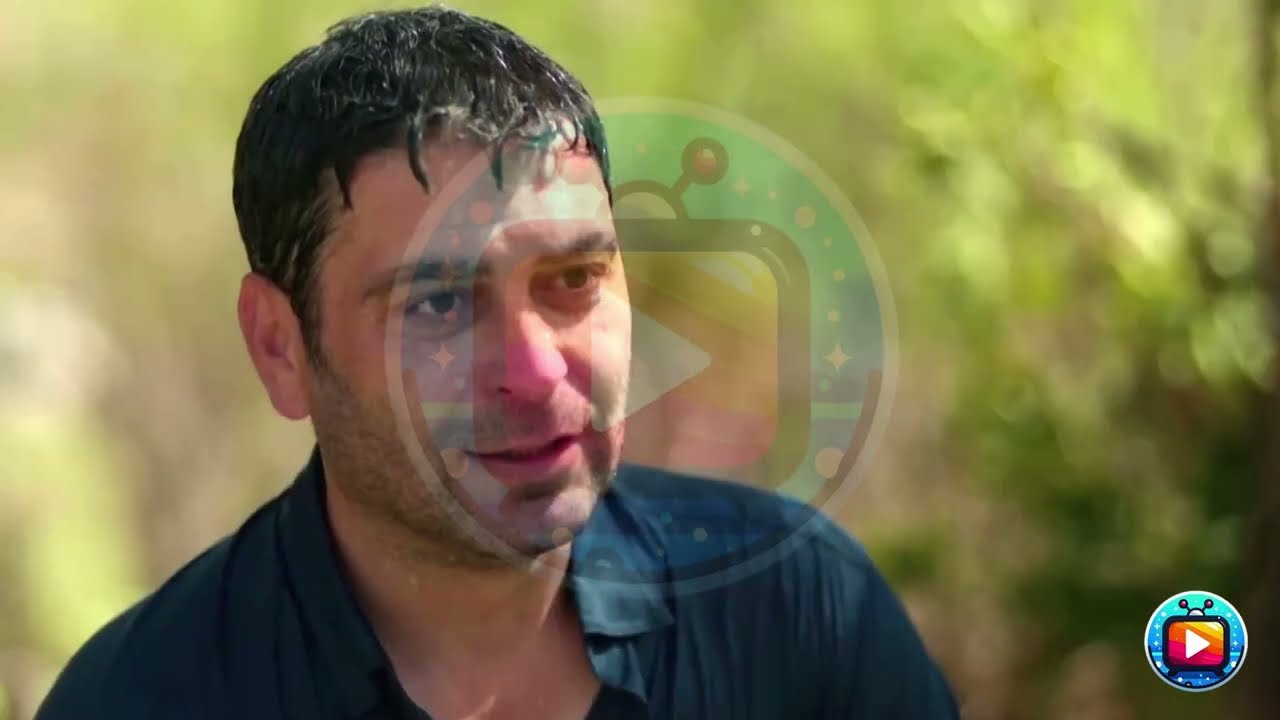 Primo piano di un uomo con il volto bagnato e lo sguardo abbassato, in camicia scura, davanti a un giardino sfocato