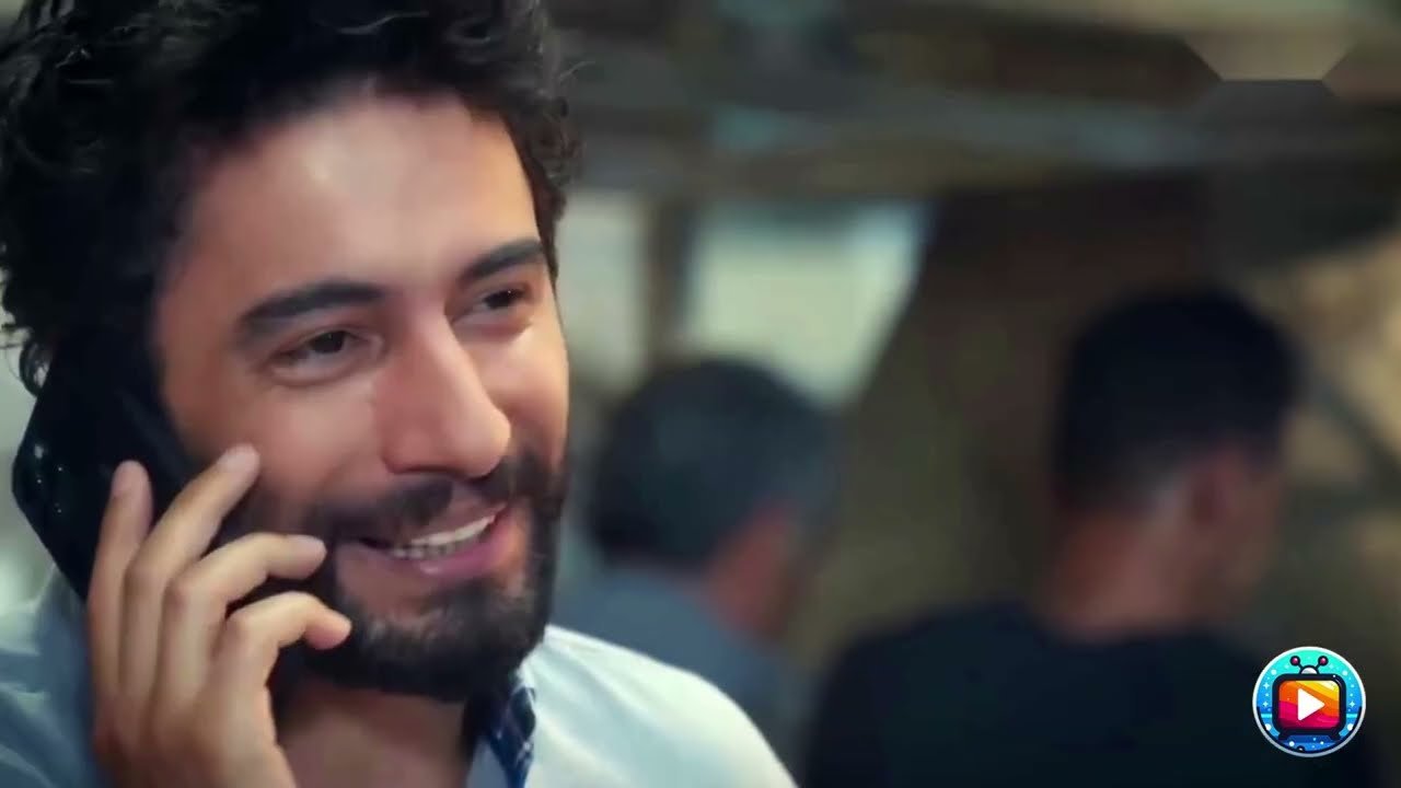 Un uomo con la barba e i capelli scuri e ricci sorride parlando al cellulare, la mano accostata al viso, camicia chiara; sullo sfondo sfocato due uomini di spalle, in un ambiente che sembra un laboratorio. In basso a destra il logo tondo di un canale.